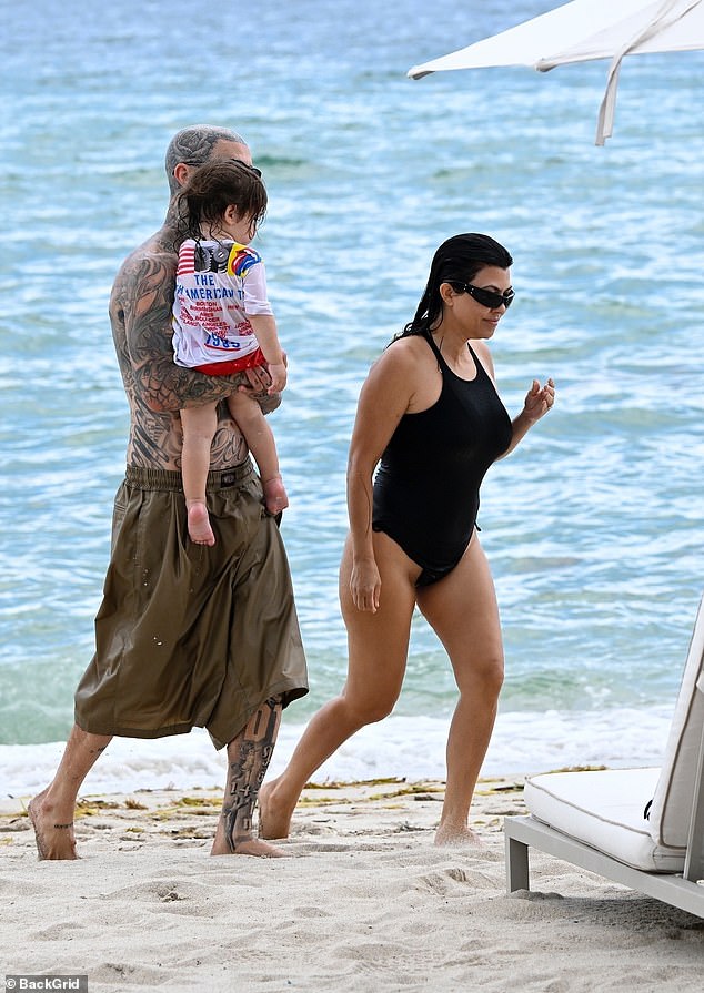 Travis looked every bit the proud papa as he carried his youngest son around for the family beach day
