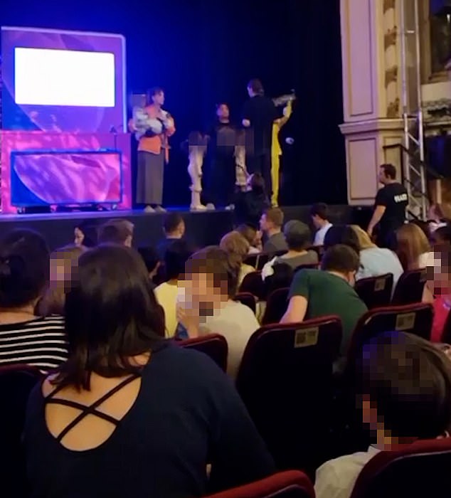 A woman, carrying a baby appears on stage during a protest at the New Wimbledon Theatre