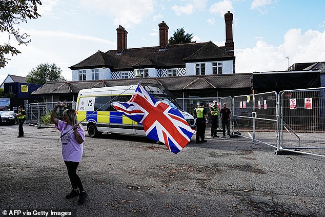 Police officers secure the area as a protester dubbed one of the 'Pink Ladies' hold a union flag outside the Bell Hotel in Epping on August 29