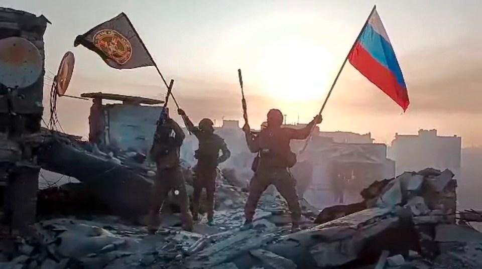 Wagner Group mercenaries raising Russian and Wagner flags on a damaged building in Bakhmut, Ukraine.