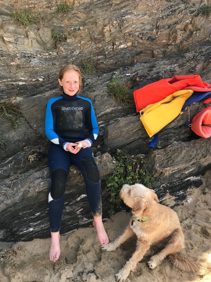 Girl in wetsuit sitting on rocks with dog.