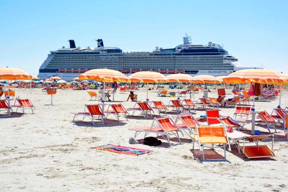 Beach with lounge chairs and umbrellas, cruise ship in background.