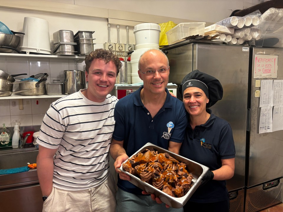 Two men and a woman holding a container of chocolate gelato in a kitchen.