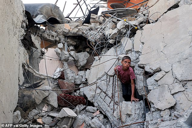 A boy climbs from out of the rubble of a collapsed building that was hit by bombardment in the Nuseirat camp for Palestinian refugees in the central Gaza Strip on August 30, 2025
