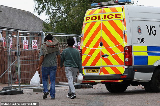 Hotel residents walk past Police Van as they arrive at The Bell Hotel, Epping, Essex