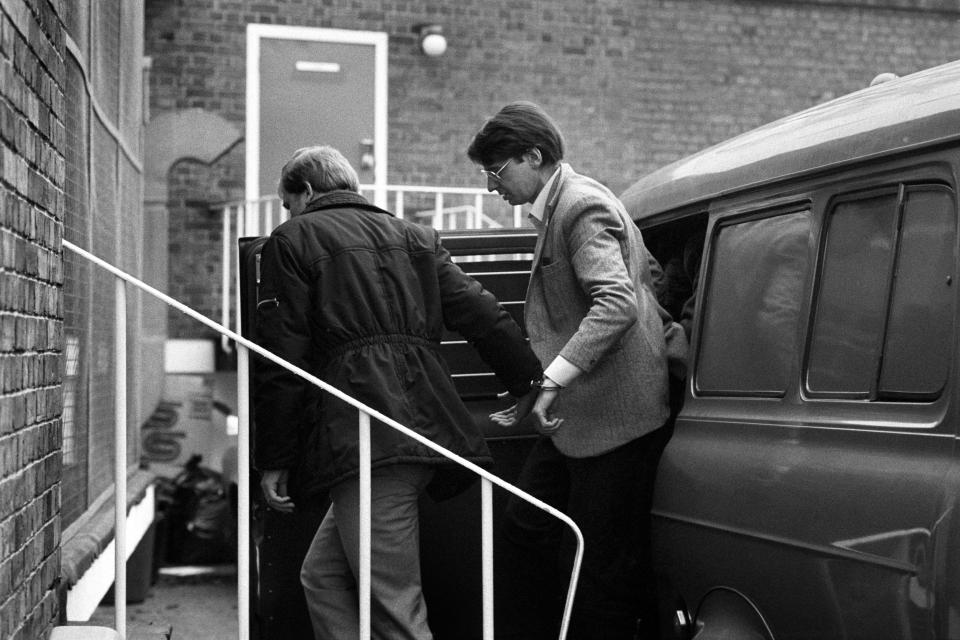 Dennis Nilsen in handcuffs being escorted to a vehicle.