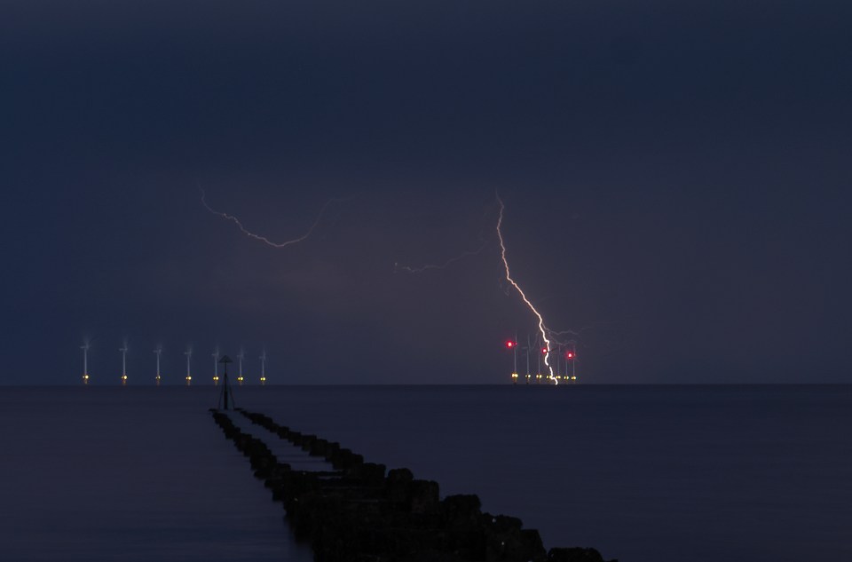 Lightning storm over the sea at night, near wind turbines.