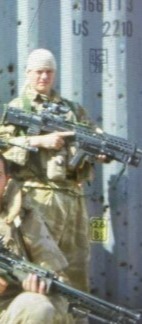 Two soldiers posing with large weapons in front of a bullet-ridden container.