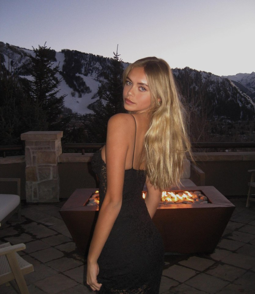 Woman in black dress on patio with fire pit and mountain view.