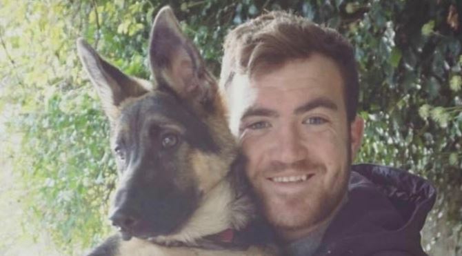 A man smiling and holding a German Shepherd puppy.