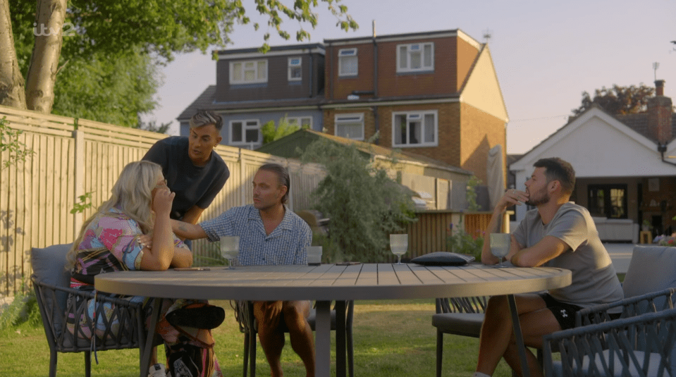 Screenshot of four people sitting at an outdoor table, one appearing upset.
