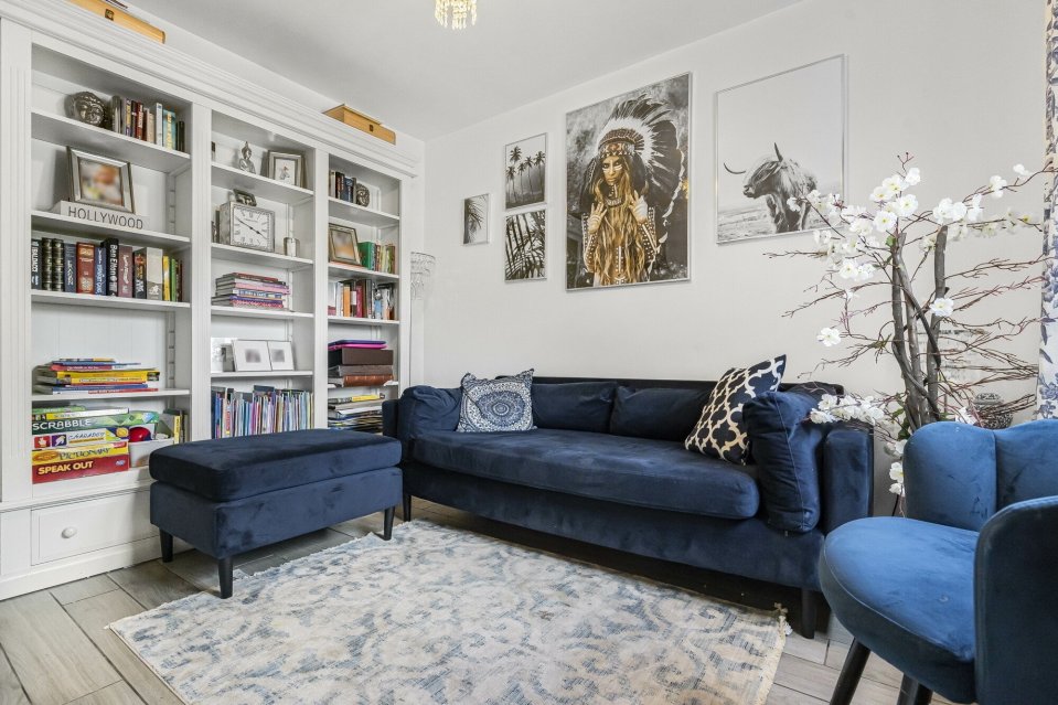 Living room with navy blue sofa and armchairs, white built-in bookcase, and wall art.