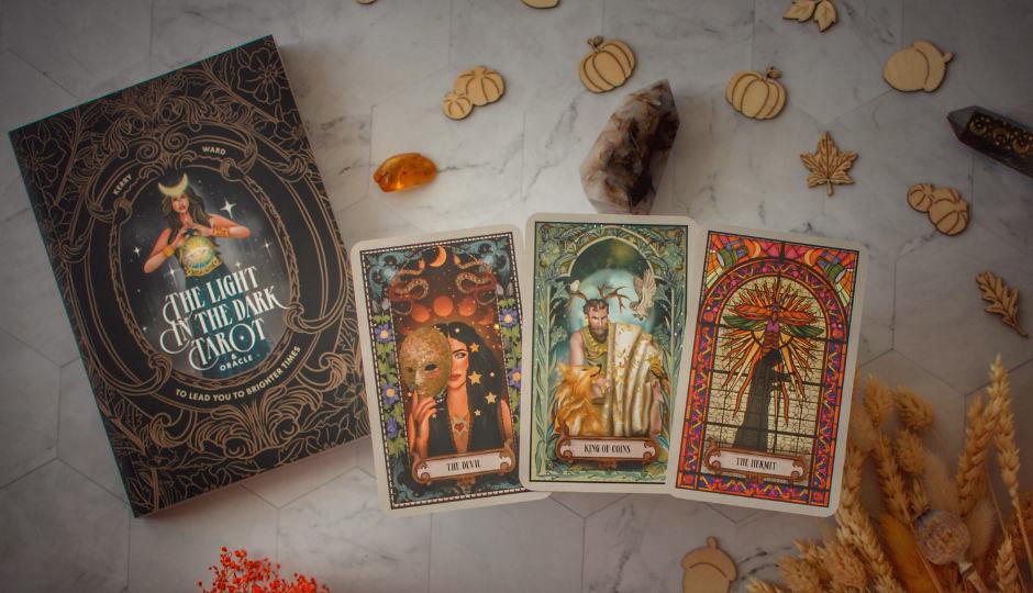 Tarot cards: The Devil, King of Coins, and The Hermit, with "The Light in the Dark Tarot" book.