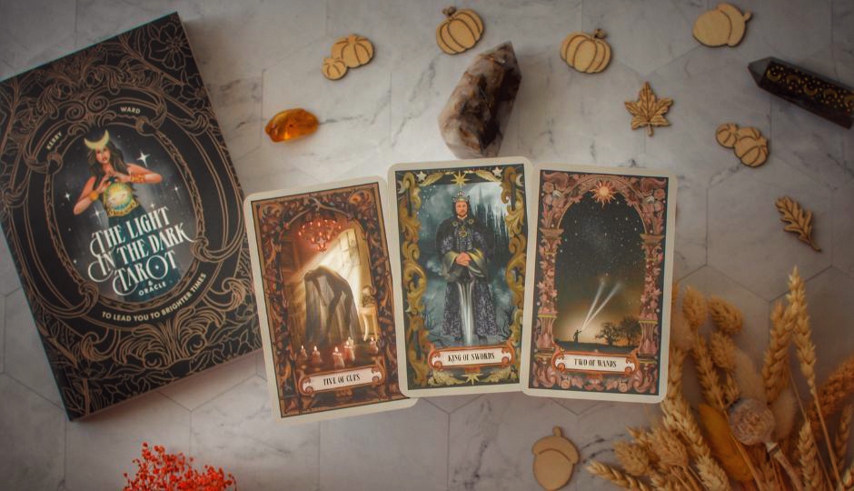 Three tarot cards from The Light in the Dark Tarot deck: Five of Cups, King of Swords, and Two of Wands.