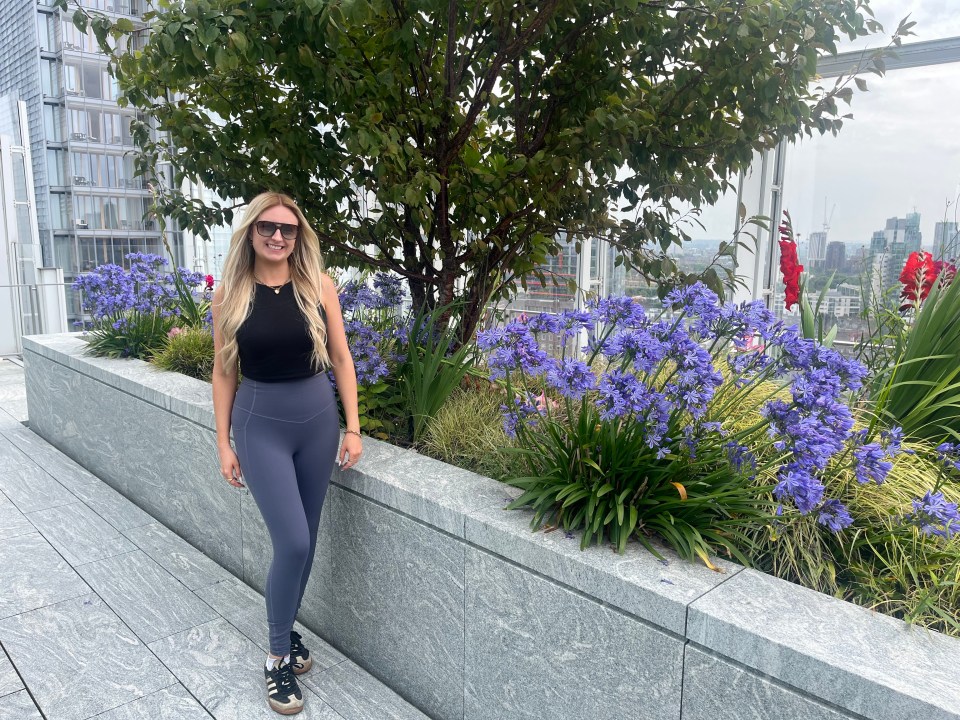 Woman in athletic wear standing by a planter with purple flowers.