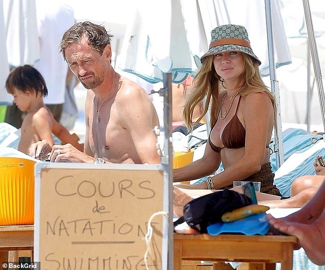 Abbey Clancy, 39, flashed her svelte physique in a gold skimpy bikini as she enjoyed a day at the beach in the south of France with her shirtless husband Peter Crouch, 44, on Tuesday