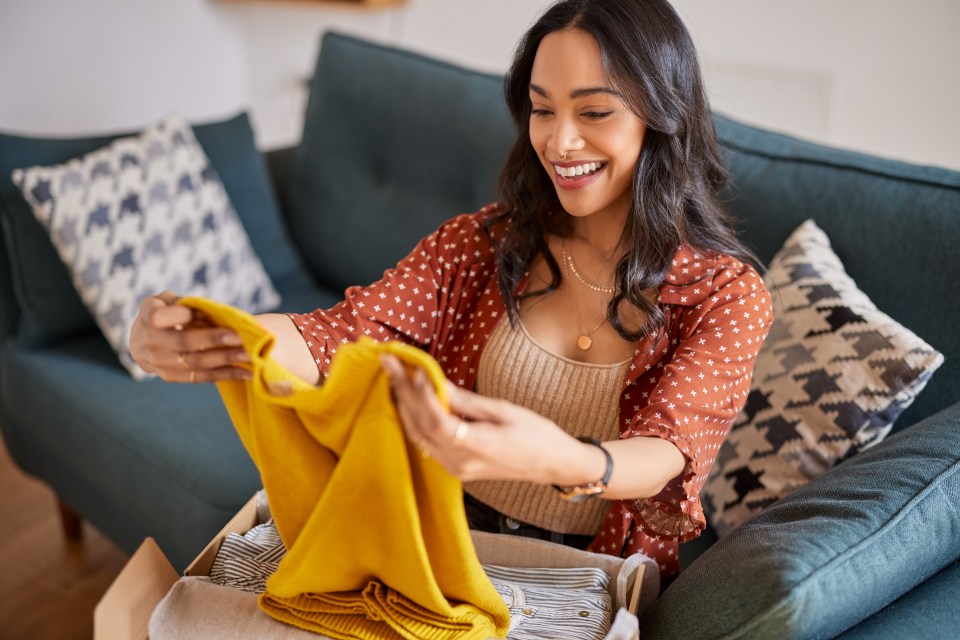 Smiling woman unpacking a yellow sweater from a box.