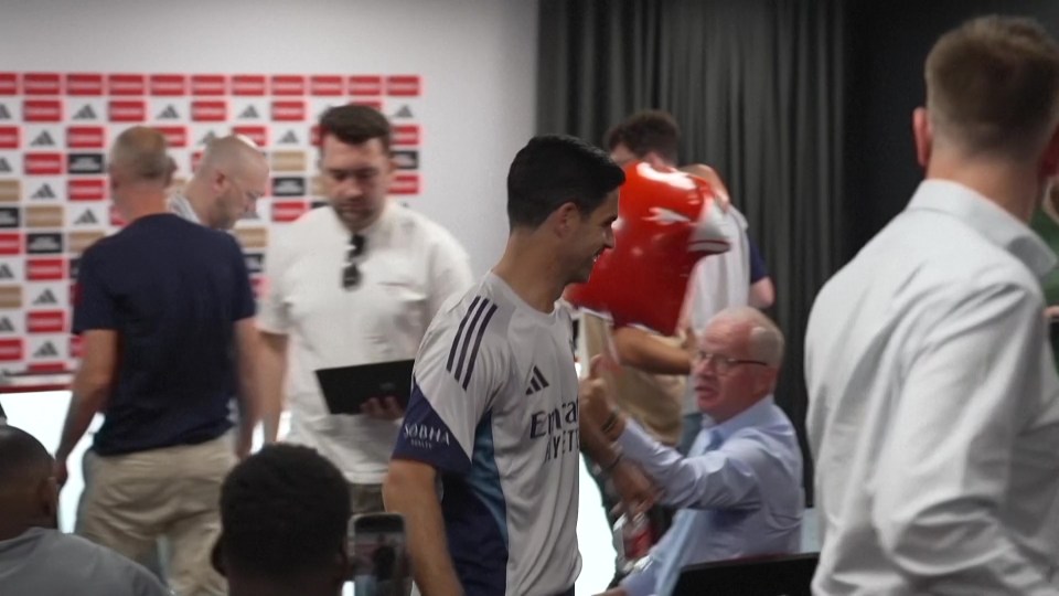 A soccer player in a white jersey high-fives someone in a room full of people.