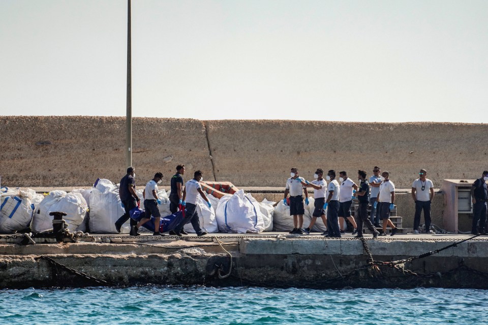 Coast guard officers carrying a body bag on a dock.