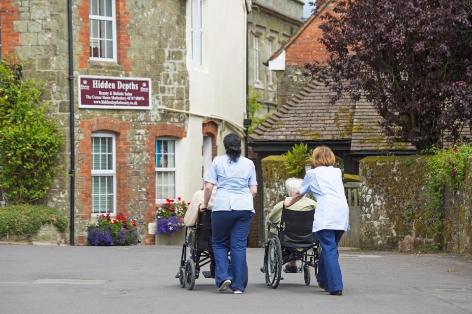 Two caregivers pushing elderly people in wheelchairs.