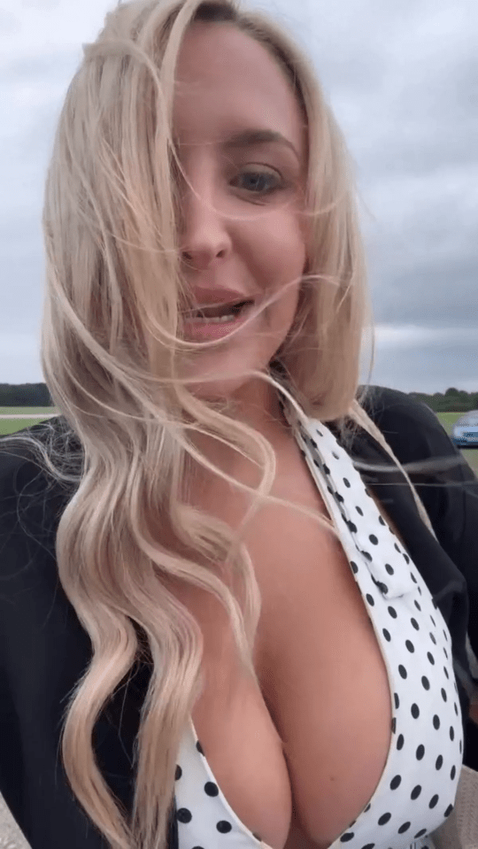 Woman with blonde hair blowing in the wind, wearing a white polka dot top.