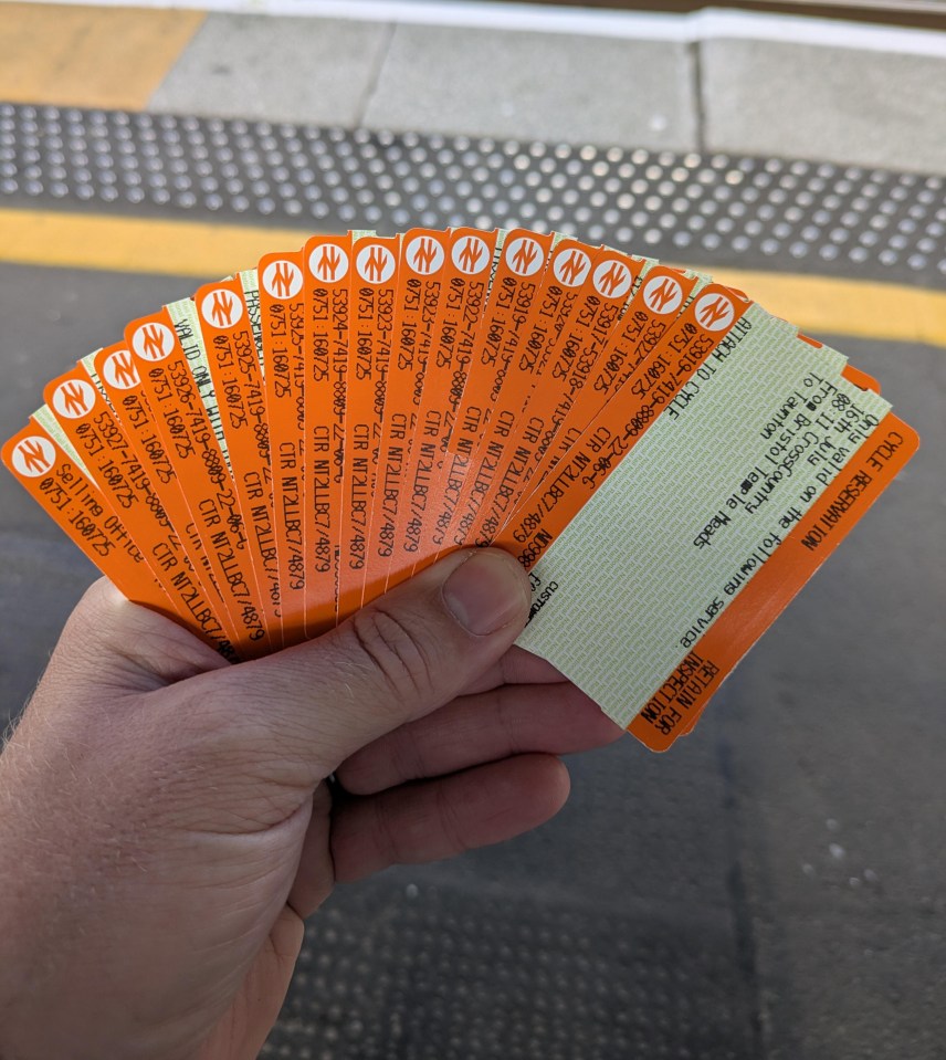 Hand holding several orange train tickets.