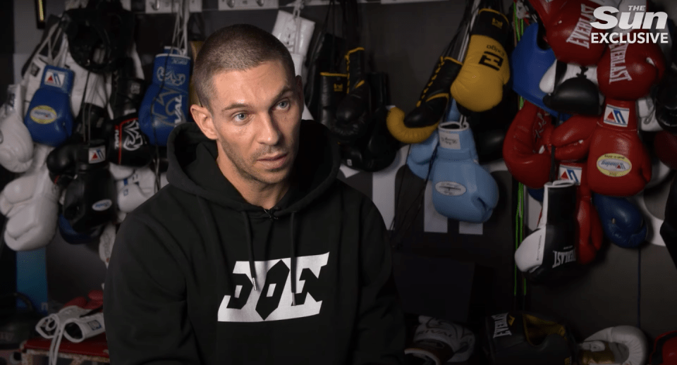 Man in black hoodie sits for interview in boxing gym.