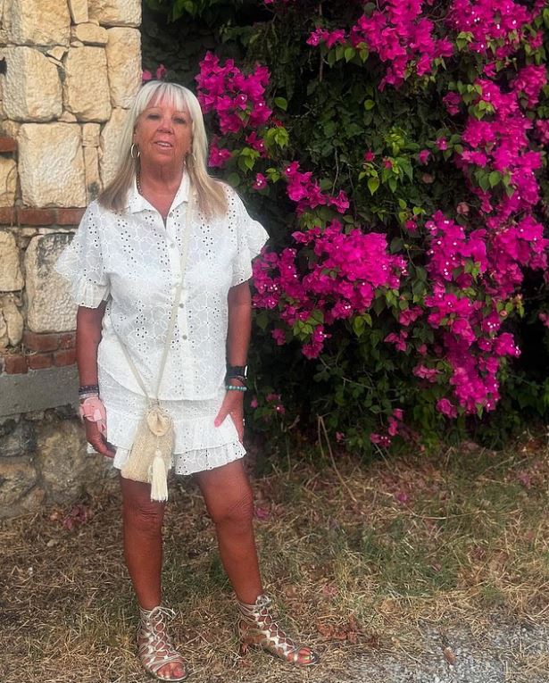 Woman in white eyelet dress standing by pink flowers.