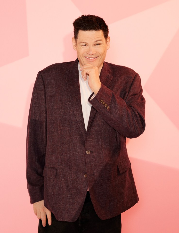 Mark Labbett from Celebs Go Dating, smiling and touching his chin.