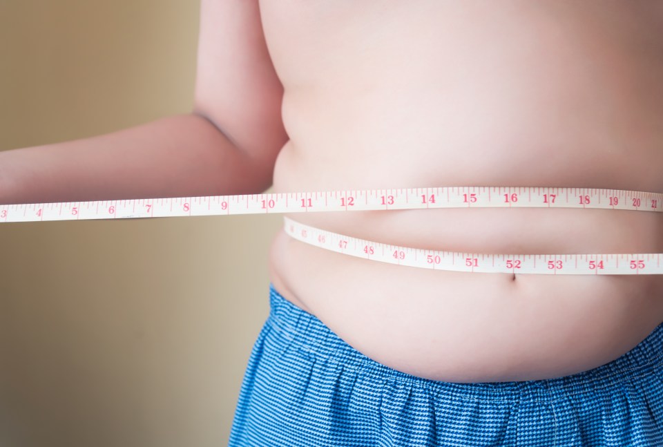 Overweight boy measuring his waist with a tape measure.