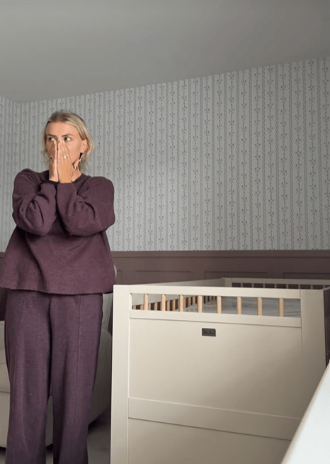 Woman in purple standing in a nursery by a crib.