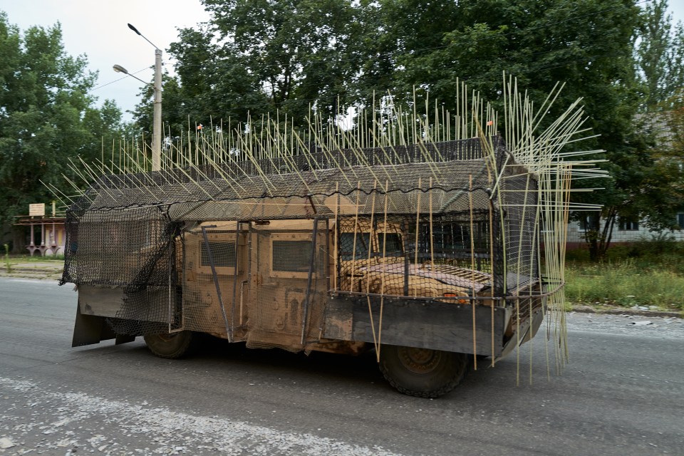 Military vehicle with cage armor driving down a road.
