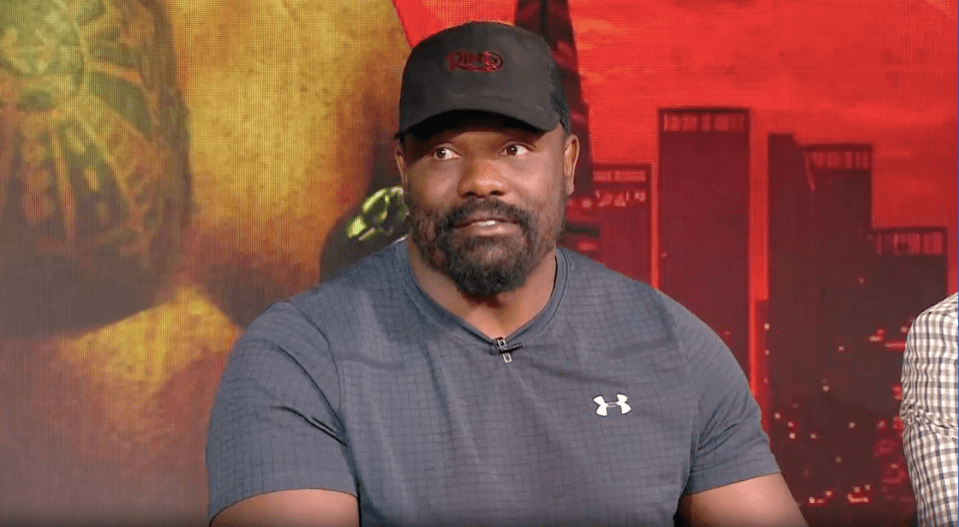 Screenshot of a man in a black baseball cap and gray shirt.