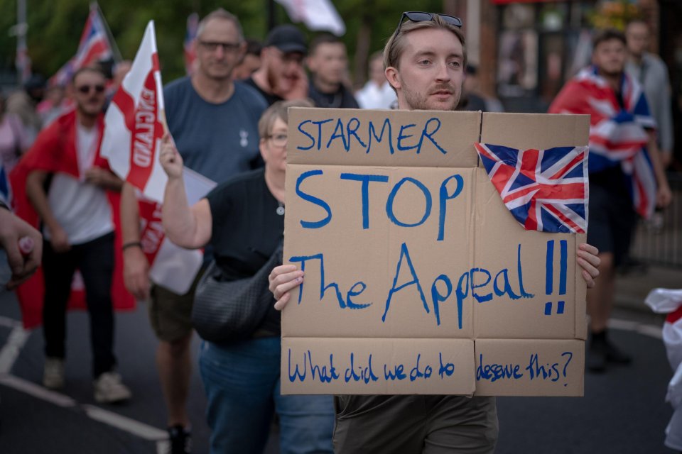 Protestor at anti-migrant march holds sign reading "Starmer Stop the Appeal!!" and "What did we do to deserve this?".