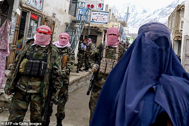 Taliban security personnel stand guard as an Afghan burqa-clad woman (R) walks along a street at a market in the Baharak district of Badakhshan province on February 26, 2024. The Taliban rules under Sharia law - a harsh Islamic legal system which permits flogging and the death penalty in some circumstances