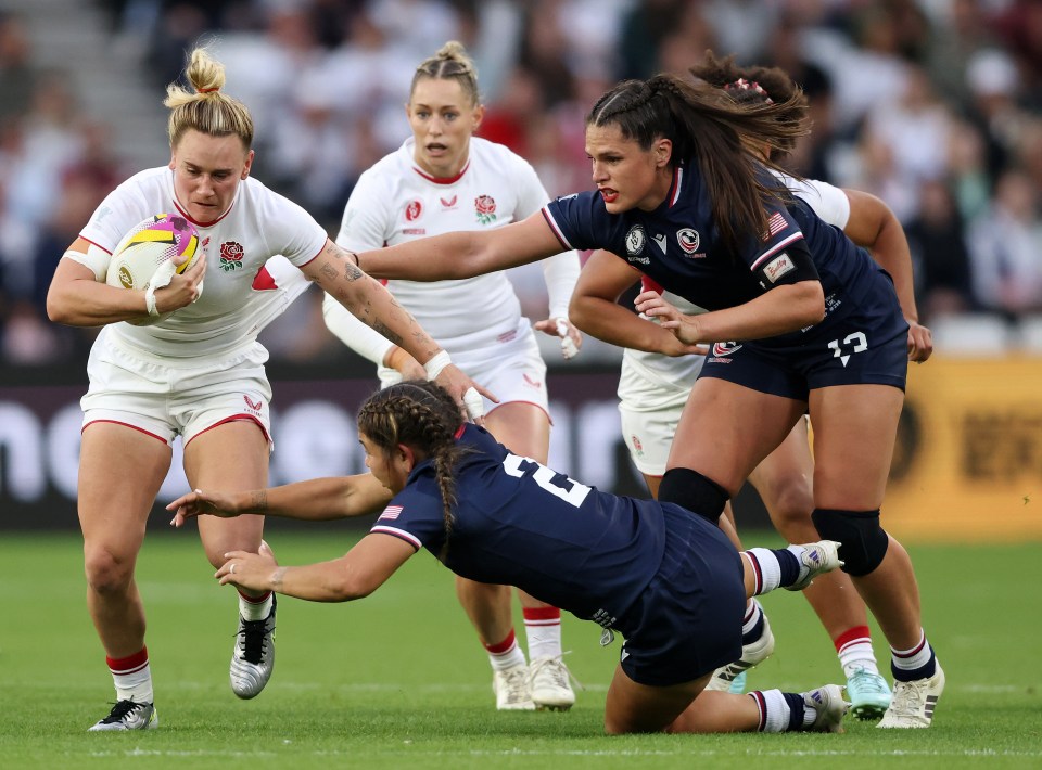Women's rugby match: England player tackled by USA players.