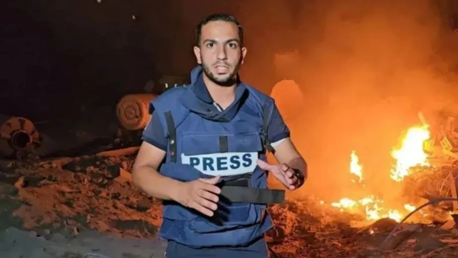 Journalist in a press vest reporting amidst a fire.