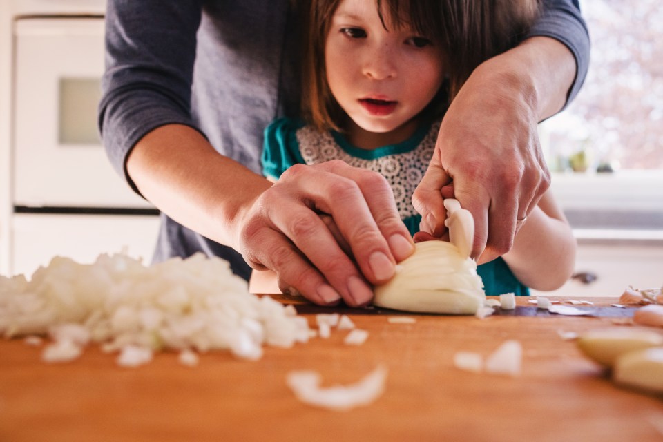 A mother teaches her young daughter to chop an onion.