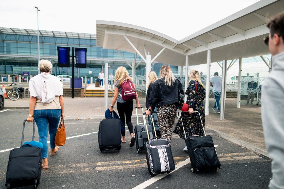 Group of women pulling suitcases toward an airport.