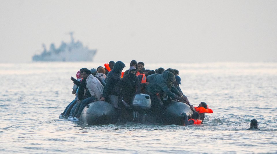 Migrants struggling to board an inflatable boat in rough seas.