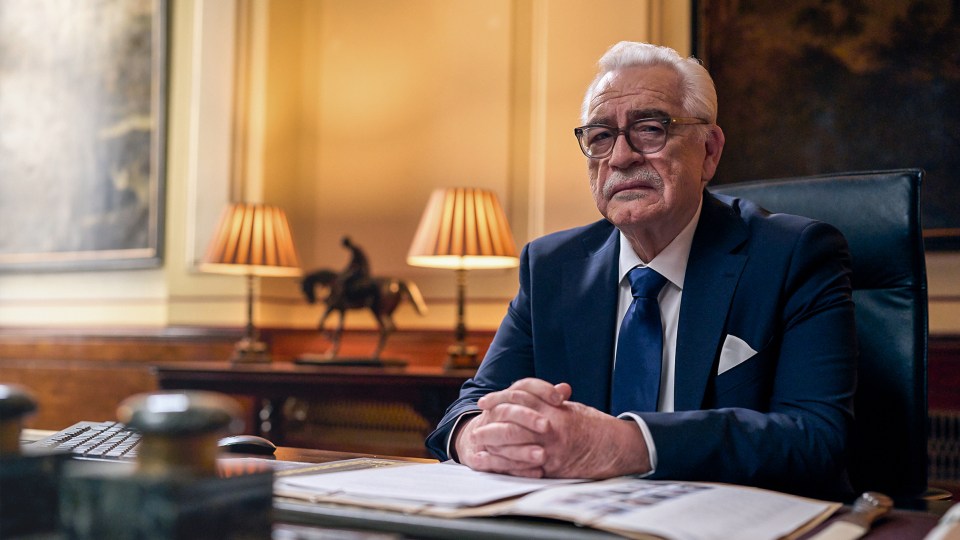 Older man in suit sitting at a desk.