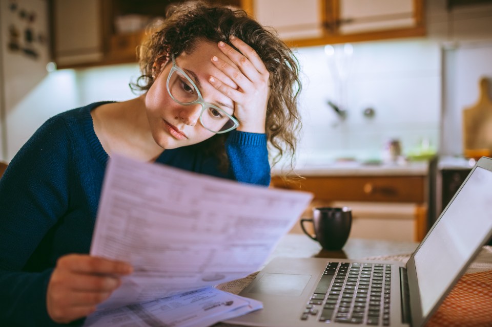 Woman looking stressed while reviewing bills at her laptop.