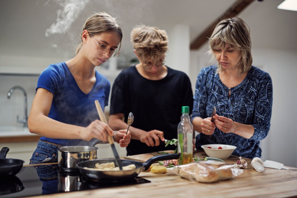 A mother and her two teenagers prepare lunch together in the kitchen.