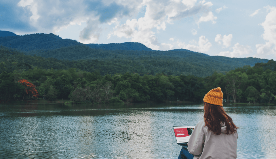 Woman using laptop overlooking lake and mountains.