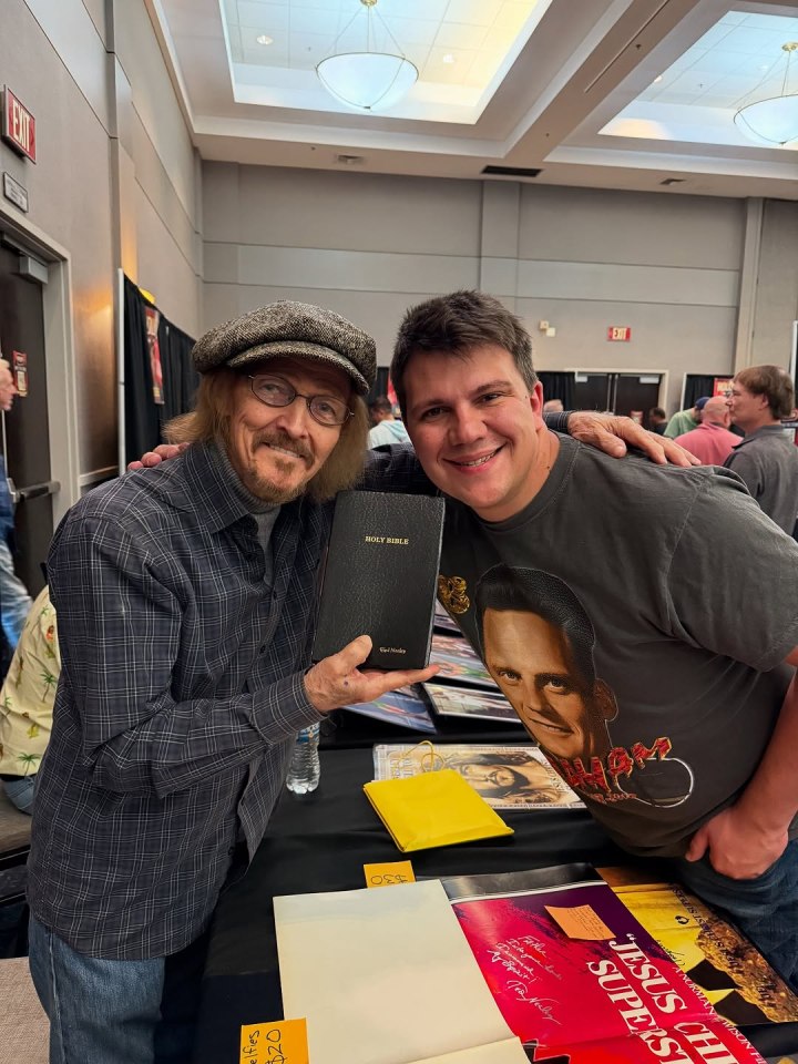 A man holding a Bible poses for a photo with a fan.