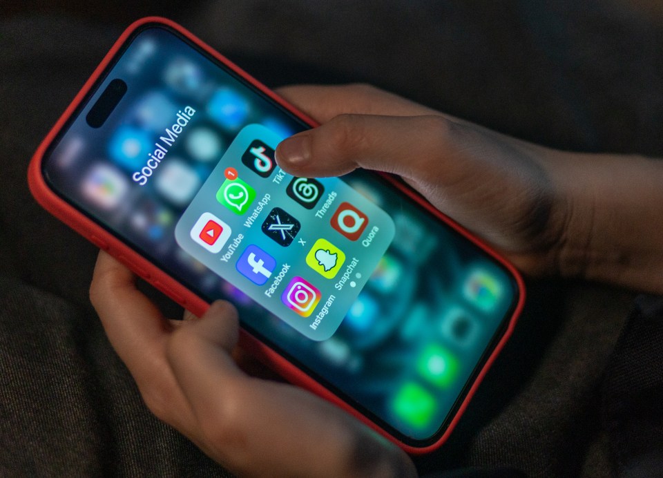 A child's hands holding an iPhone displaying various social media apps.