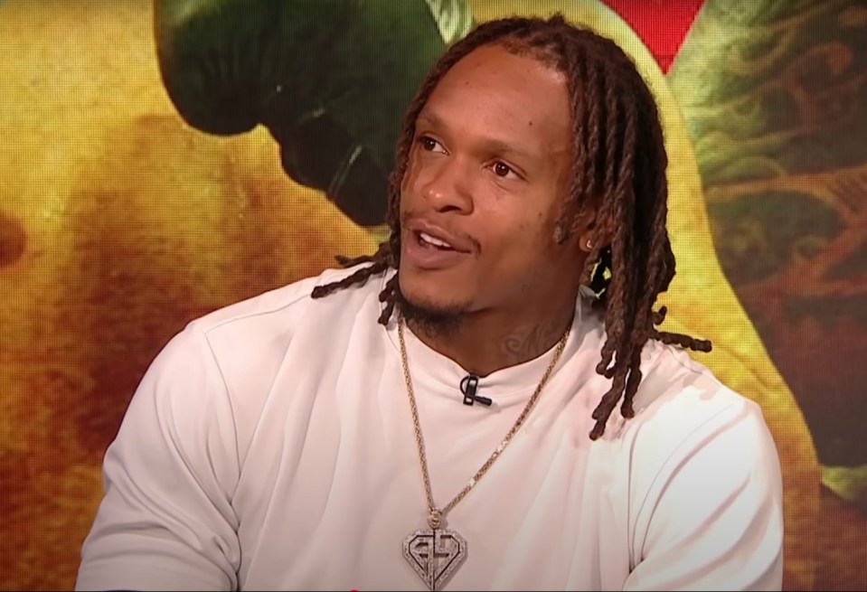 Man with long dreadlocks in a white shirt on a DAZN broadcast.