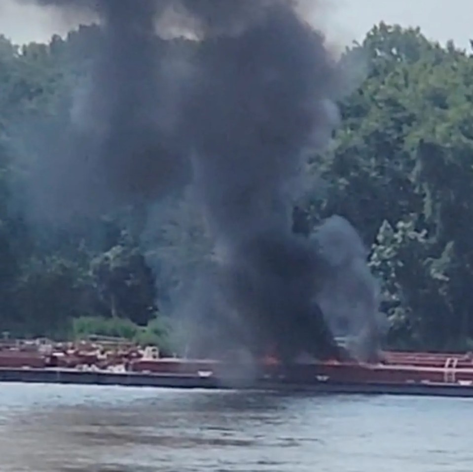 Smoke rising from a barge fire on a river.