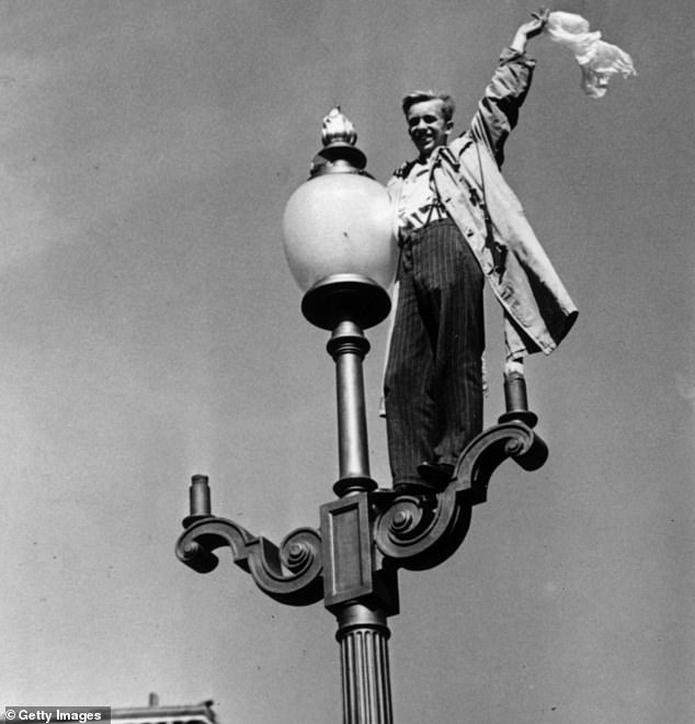 A man waving from a lamppost to the crowds below in Piccadilly Circus, London, during the celebrations following the news of Japan's surrender, August 10, 1945