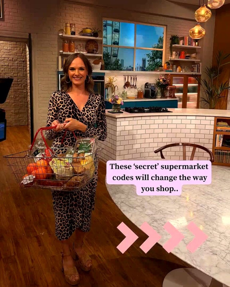 Woman holding a shopping basket with groceries, in a kitchen setting.